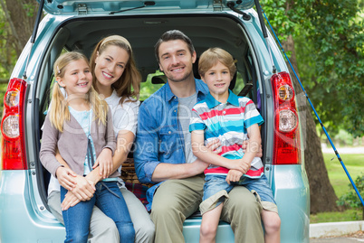 Portrait of happy family of four sitting in car trunk