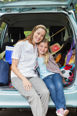 Smiling mother and daughter sitting in car trunk