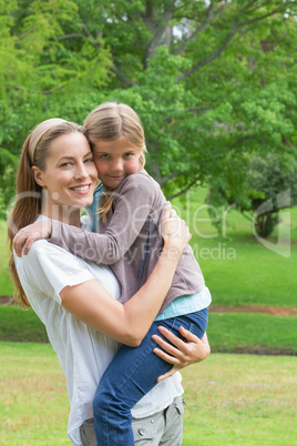 Smiling mother carrying daughter at park