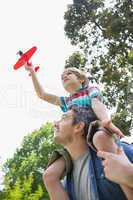 Boy with toy aeroplane sitting on father's shoulders