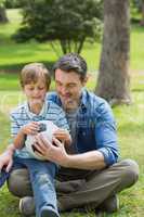 Father and son sitting with ball at park