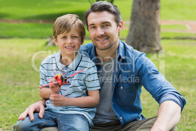 Boy with toy aeroplane sitting on father's lap at park