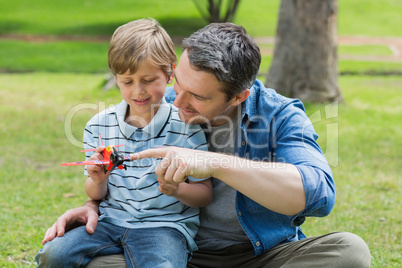 Boy with toy aeroplane sitting on father's lap at park