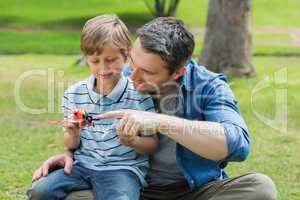 Boy with toy aeroplane sitting on father's lap at park