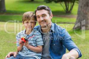 Boy with toy aeroplane sitting on father's lap at park