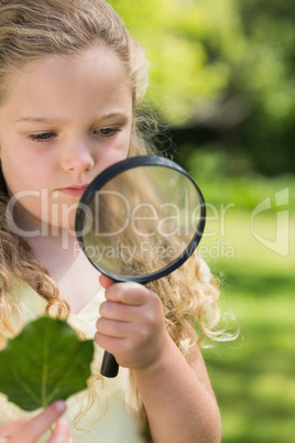 Girl holding leaf and magnifying glass at park