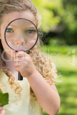 Cute girl looking through magnifying glass at park