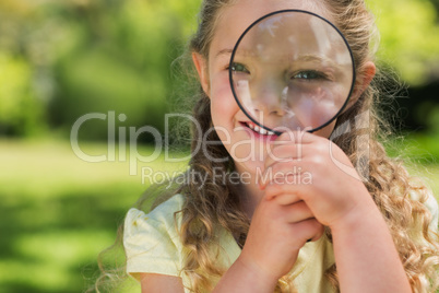 Cute girl looking through magnifying glass at park