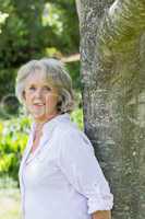 Portrait of mature woman leaning against tree trunk