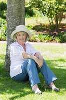 Mature woman sitting against a tree in park