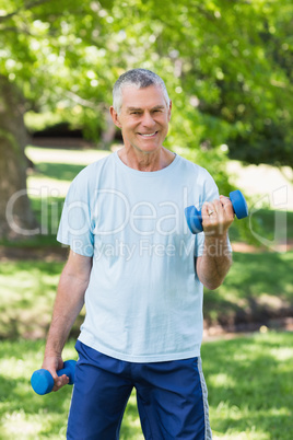 Smiling mature man with dumbbells at park