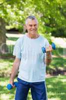 Smiling mature man with dumbbells at park