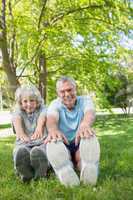 Mature couple stretching hands to legs at park