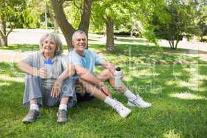 Mature couple sitting with water bottles at park