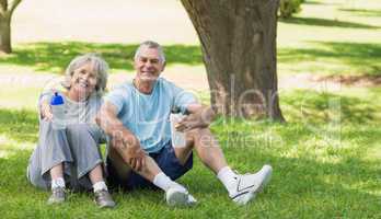 Smiling mature couple sitting with water bottles at park