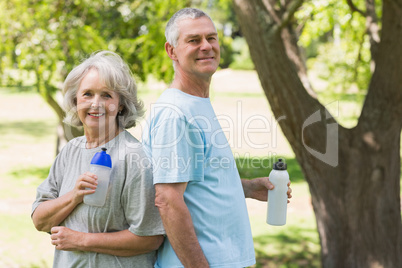 Mature couple standing with water bottles at park