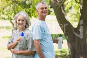 Mature couple standing with water bottles at park