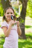Smiling girl holding leaves and magnifying glass at park