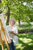 Smiling mature woman painting on canvas in park