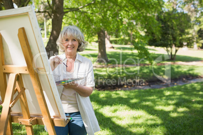 Smiling mature woman painting in park