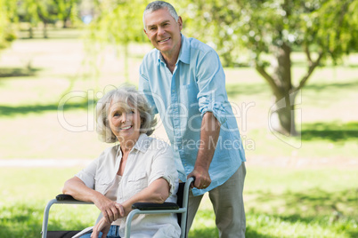 Mature man with woman sitting in wheel chair at park
