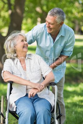 Mature man with woman sitting in wheel chair at park
