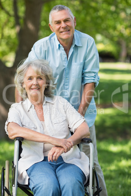 Mature man with woman sitting in wheel chair at park