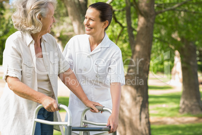 Woman assisting mature female with walker at park