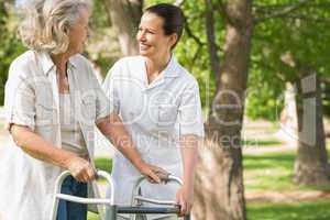 Woman assisting mature female with walker at park