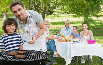 Father and son at barbecue grill with family having lunch in par