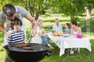 Father and son at barbecue grill with family having lunch in par