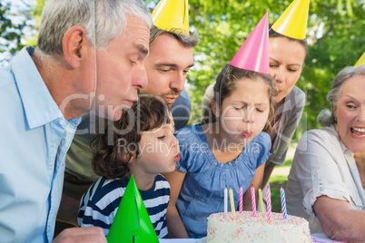 Extended family in party hats blowing birthday cake