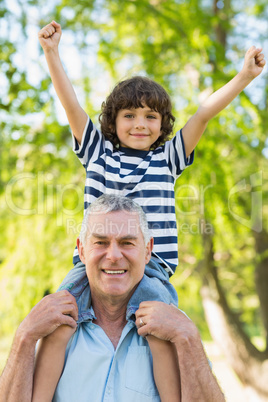 Grandfather carrying son on shoulders at park