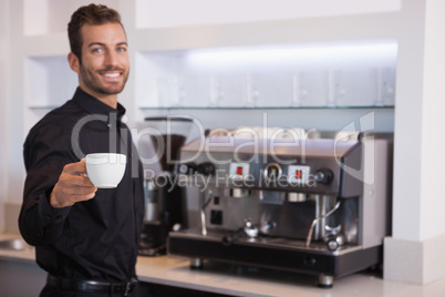 Handsome barista offering a cup of coffee to camera