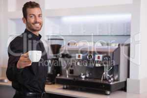 Handsome barista offering a cup of coffee to camera