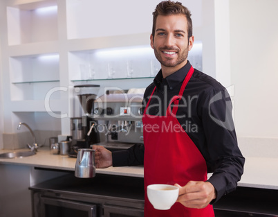 Handsome young barista holding jug and cup of coffee