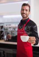 Smiling young barista holding jug and cup of coffee