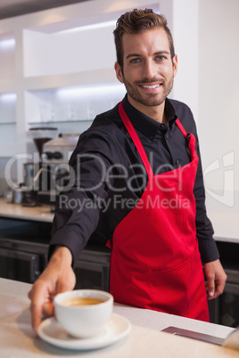 Smiling young barista putting cup of coffee down on counter