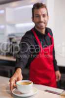 Happy young barista putting cup of coffee down on counter
