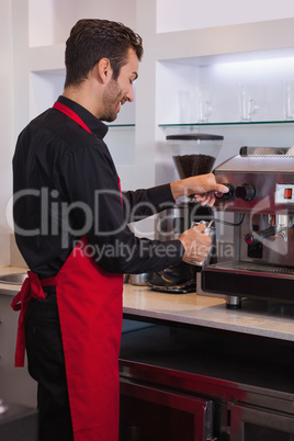 Happy young barista steaming jug of milk