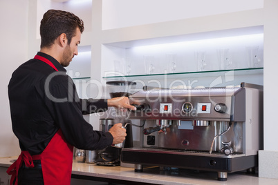 Handsome young barista steaming jug of milk