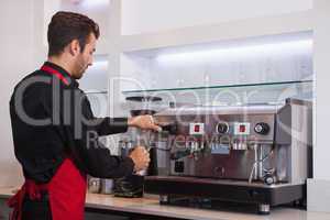 Handsome young barista steaming jug of milk