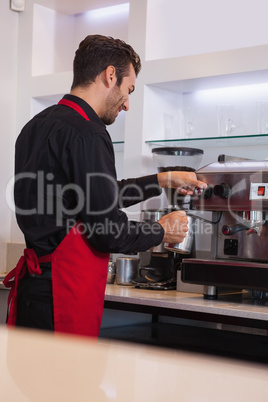 Smiling young barista steaming jug of milk