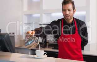 Smiling barista pouring milk into cup of coffee