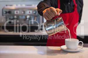 Barista pouring milk into cup of coffee