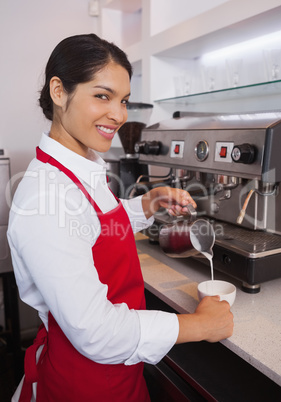 Pretty barista pouring milk into cup of coffee