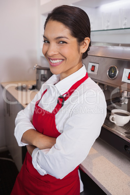 Pretty young barista leaning against counter smiling at camera
