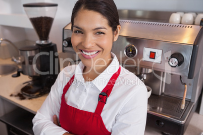 Happy young barista leaning against counter smiling at camera