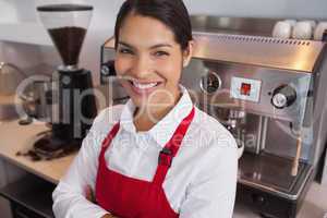 Happy young barista leaning against counter smiling at camera