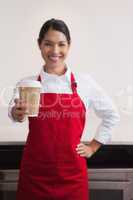 Happy young barista offering cup of coffee to go